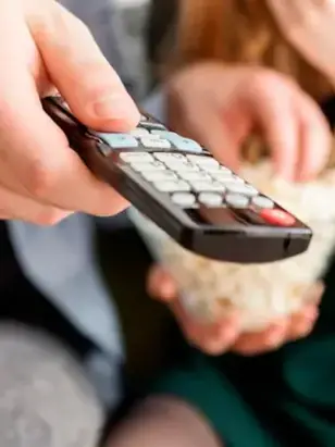 Mão segurando o controle remoto diante da TV