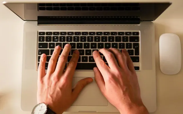 Mãos com notebook e relógio no escritório